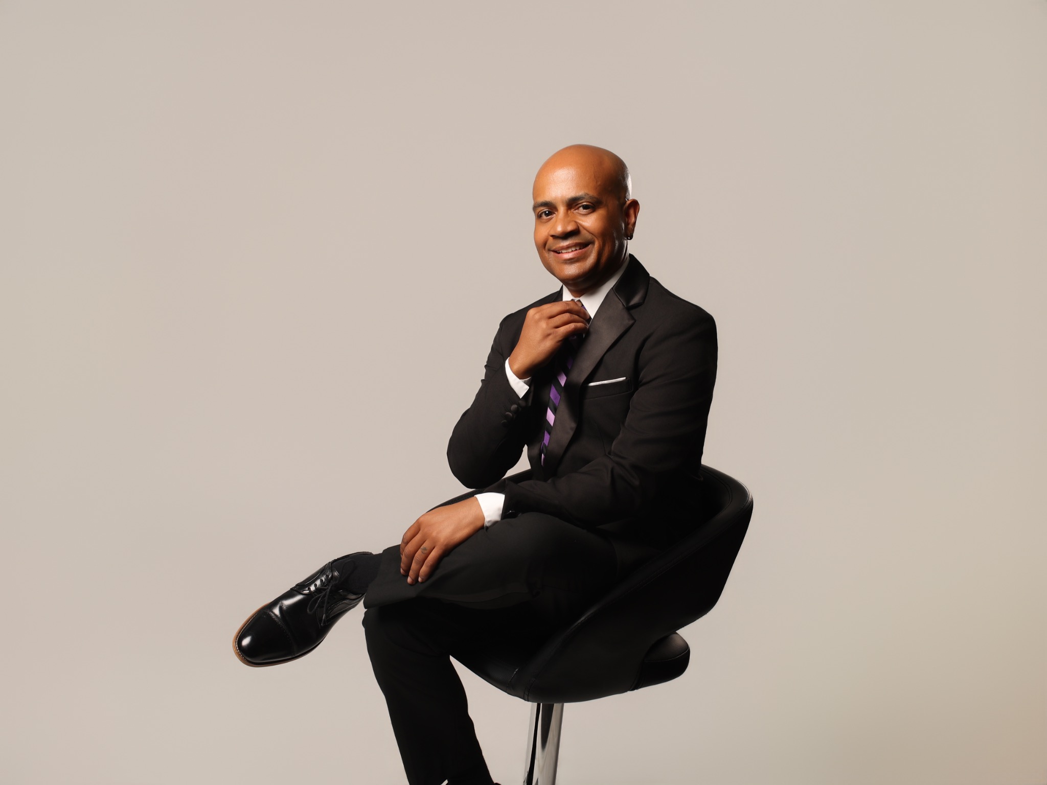 Eric Velez seated in a black suit and striped tie
